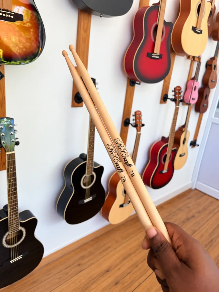 A pair of 7B drumsticks held in front of the guitar wall at Presto Forte in Thumpoly